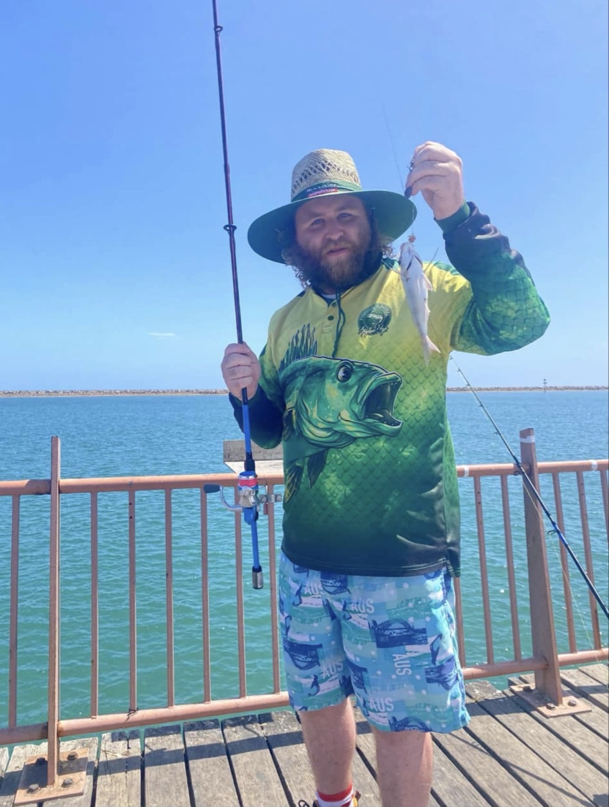 On the jetty holding a fishing rod and a freshly caught fish, ocean behind
